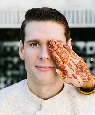 dark bridal henna hand in front of husbands left eye