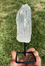 Clear quartz crystal on metal stand held above grass